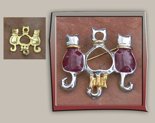 Three cats sit together in gold and shiny silver metal with burgundy enamel brooch