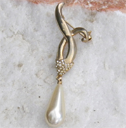 Vintage brooch features long pearl droplet on gold metal sash. 